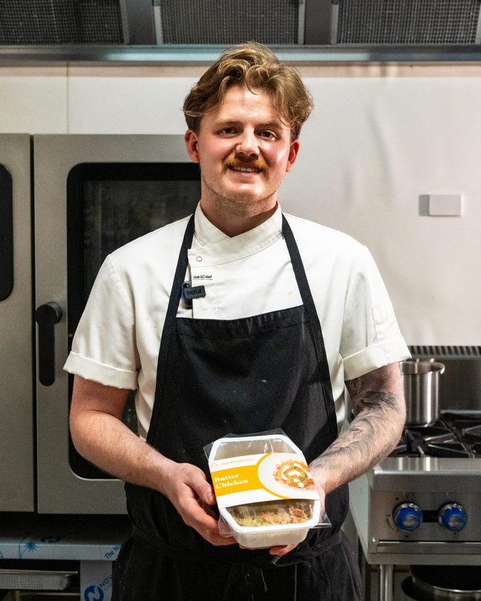 Lachlan Cook in the Gourmet2Go kitchen, holding a Butter Chicken meal